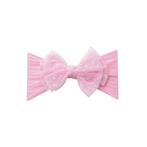 Pu&ograve; includere: Un cerchietto rosa con un grande fiocco a strati in tulle rosa con pois bianchi.