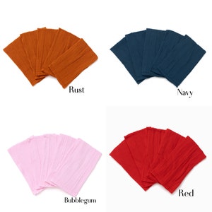 May include: Set of six fabric headbands in four colors: rust, navy, bubblegum pink, and red. The headbands are made of a textured fabric and are folded in a fan shape.