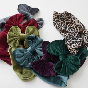 May include: A collection of velvet headbands with bows in various colors, including burgundy, teal, green, and olive green. One headband features a leopard print.