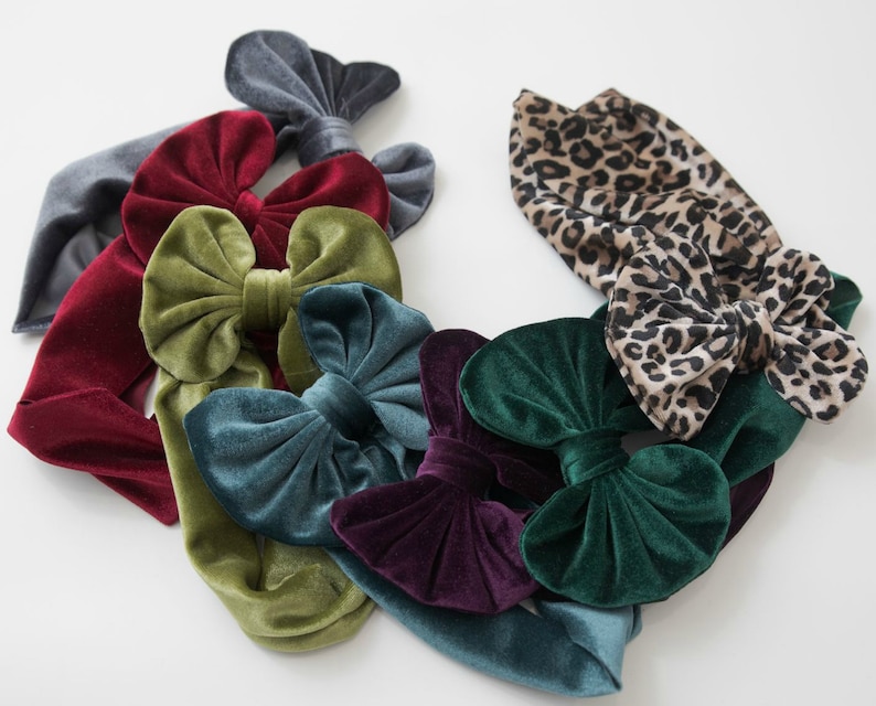 May include: A collection of velvet headbands with bows in various colors, including burgundy, teal, green, and olive green. One headband features a leopard print.