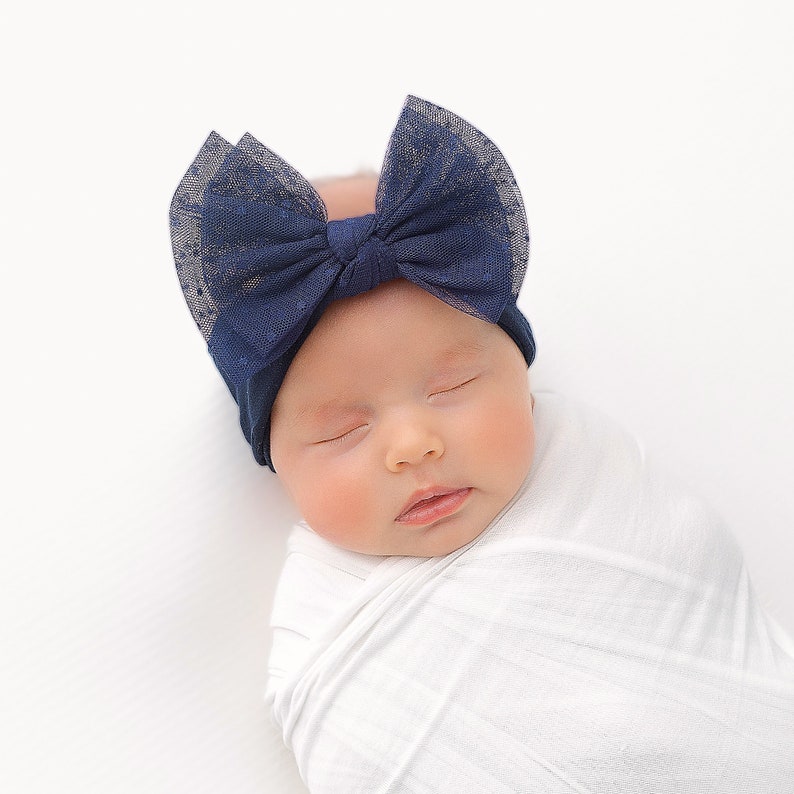 Pu&ograve; includere: Un bambino che dorme con un cerchietto blu scuro con un fiocco e una copertina bianca.