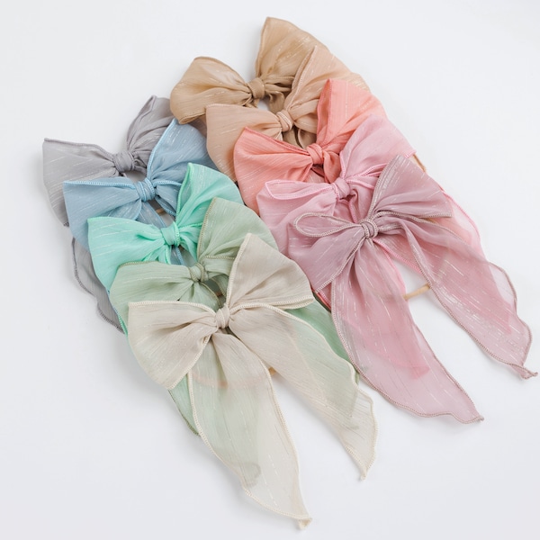Puede incluir: Un conjunto de ocho lazos para el pelo de color pastel con colas largas. Los lazos están hechos de tela transparente con un acabado brillante. Los colores incluyen azul claro, verde menta, melocotón, rosa claro, beige y un tono de rosa más oscuro.