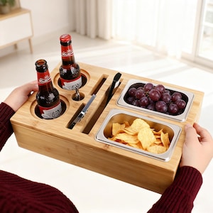 May include: A bamboo serving tray with two beer bottles, two stainless steel containers holding grapes and chips, and slots for utensils. The tray is designed for snacks and drinks.