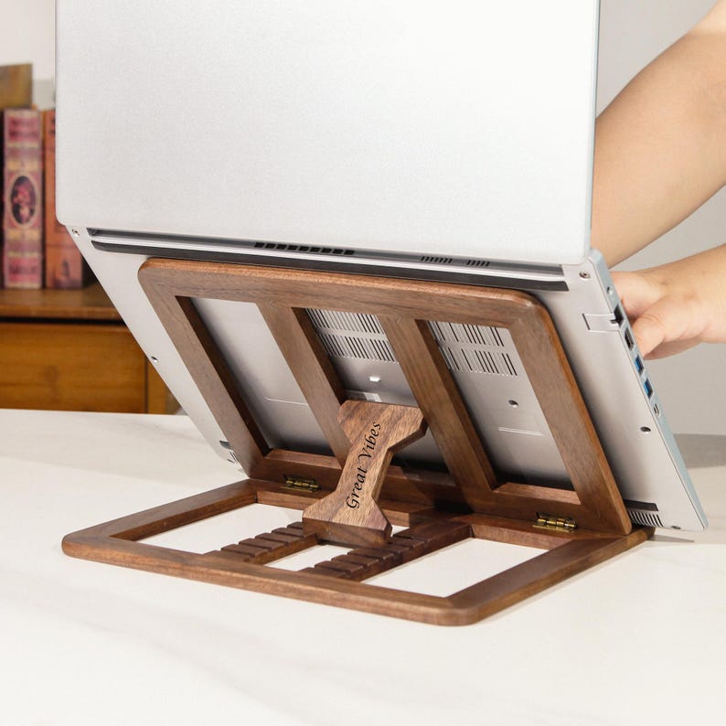 May include: A wooden laptop stand with a natural finish. The stand is designed to elevate a laptop for improved ergonomics. The text "Great Vibes" is engraved on the front. The stand is made of wood and has a foldable design.