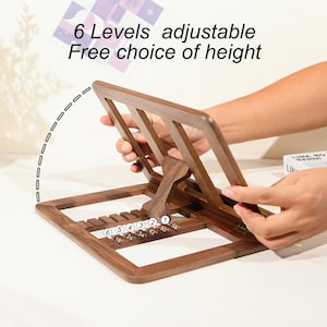 May include: A wooden adjustable book stand with six height levels. The stand is brown and features the text "6 Levels adjustable Free choice of height". The stand is being adjusted by a person's hands.