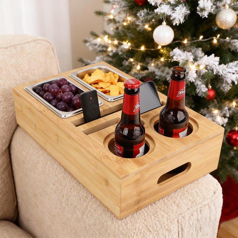 May include: A bamboo sofa arm tray with two drink holders, two stainless steel food trays, and slots for a remote and a phone. The tray holds two bottles of beer, grapes, and chips. A Christmas tree is in the background.