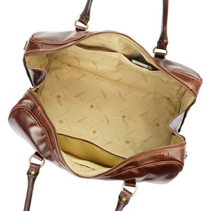 Puede incluir: Bolso de viaje de cuero marr&oacute;n abierto con cierre de cremallera. El interior beige tiene varios bolsillos y un tel&eacute;fono. El bolso tiene dos asas y herrajes dorados. El cuero tiene un acabado brillante.