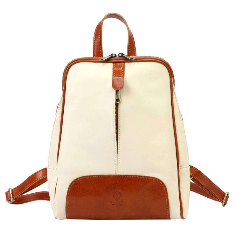 May include: Cream-colored leather backpack with brown leather accents. Features a front pocket, top handle, and adjustable straps. The backpack has a zipper closure and a small brown leather detail on the zipper.