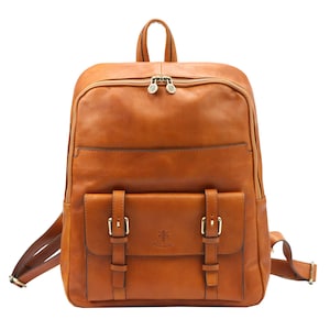 Peut inclure: Un sac à dos en cuir marron avec une poche avant fermée par deux sangles et boucles. Il possède une poignée supérieure, des bretelles réglables et un compartiment principal zippé. Le cuir est de couleur chaude.