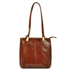 Peut inclure: Un sac fourre-tout en cuir marron avec de longues anses et des ferrures dorées. Le sac est de forme rectangulaire avec une fermeture éclair et un petit logo en bas à droite. Le cuir a une finition brillante.