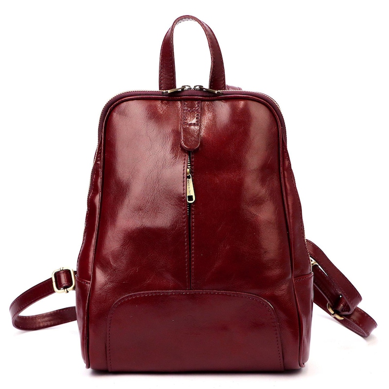 May include: A burgundy leather backpack with a top handle and adjustable shoulder straps. The backpack has a front pocket, a zipper closure, and gold-colored hardware. The bag is approximately 12 inches tall and 10 inches wide.