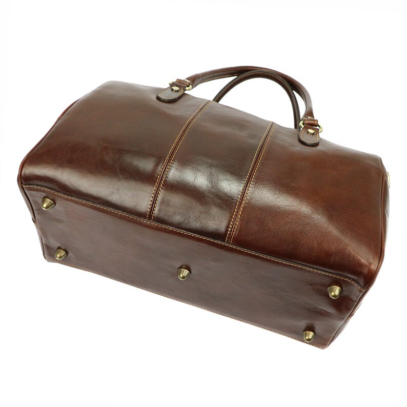 Puede incluir: Una bolsa de lona de cuero marr&oacute;n con un acabado brillante. La bolsa tiene dos asas superiores, una correa para el hombro y pies de color lat&oacute;n. Las costuras son de color marr&oacute;n claro y la bolsa tiene forma rectangular.