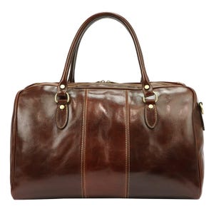 Puede incluir: Un bolso de viaje de cuero marr&oacute;n con dos asas superiores y cierre de cremallera. El bolso tiene un acabado brillante y herrajes dorados. Se ven detalles de costuras verticales en la parte delantera. Dise&ntilde;ado para viajes.