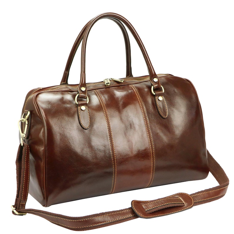 Puede incluir: Bolso de viaje de cuero marr&oacute;n brillante con correa de hombro desmontable y dos asas superiores. El bolso presenta detalles dorados, incluyendo la cremallera y las fijaciones de la correa. Dise&ntilde;o cl&aacute;sico y adecuado para viajes, con un aspecto pulido.