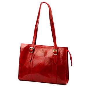 May include: A glossy, red leather tote bag with two long shoulder straps. The bag features gold-coloured buckles and a small front pocket. The leather has a polished finish, reflecting light.