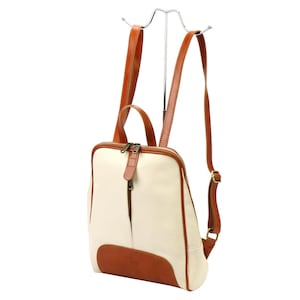 May include: Cream-colored leather backpack with brown leather accents. The backpack features a front zipper, a top handle, and adjustable shoulder straps. The bottom and trim are brown, and the hardware is silver-toned.