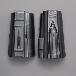 May include: Two silver-colored, cylindrical objects with detailed, geometric designs. The objects have a metallic sheen and are set against a neutral background. The design includes rectangular and triangular shapes.