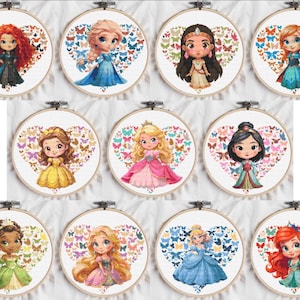 以下が含まれることがあります： 漫画のプリンセスデザインが施された、11個のクロスステッチ刺繍枠のコレクション。各プリンセスは、蝶のハート型の配置の中に配置されています。プリンセスはカラフルなドレスを着ており、ユニークなヘアスタイルで、白い布の背景に設定されています。
