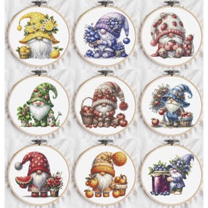 Puede incluir: Nueve aros de bordado de punto de cruz con diseños de gnomos. Cada gnomo tiene una larga barba blanca y un sombrero colorido, rodeado de frutas y flores. Los gnomos están sobre un fondo de tela blanca.
