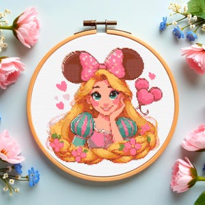 May include: A cross-stitch embroidery hoop featuring a cartoon princess with long blonde hair, wearing a pink dress and a bow. The princess is surrounded by pink hearts and flowers. The hoop is made of wood.