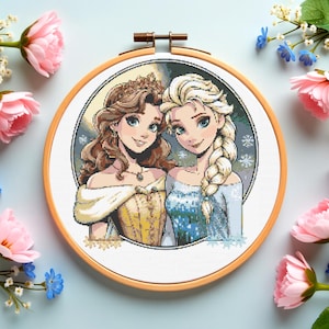 Puede incluir: Un bastidor de bordado de punto de cruz con dos personajes femeninos animados con cabello largo, uno rubio y otro moreno, en un diseño circular. El bastidor es de madera y está rodeado de flores rosas y azules.
