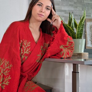 Op de afbeelding: Een rode kimono met gouden geborduurde koraalachtige patronen. De kimono heeft wijde mouwen en een gefranjerde rand. De kimono is gemaakt van een textuurstof en wordt in de taille geknoopt.