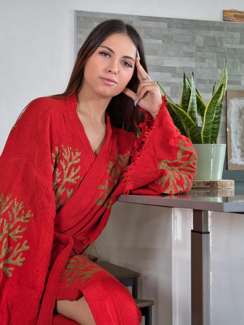 Op de afbeelding: Een rode kimono met gouden geborduurde koraalachtige patronen. De kimono heeft wijde mouwen en een gefranjerde rand. De kimono is gemaakt van een textuurstof en wordt in de taille geknoopt.
