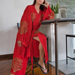 Op de afbeelding: Een rode kimono met gouden geborduurde koraalachtige ontwerpen. De kimono heeft een gefranjerde zoom en mouwen, en een bijpassende riem. De persoon draagt ​​zwarte slippers. De kimono is gemaakt van een lichte stof.