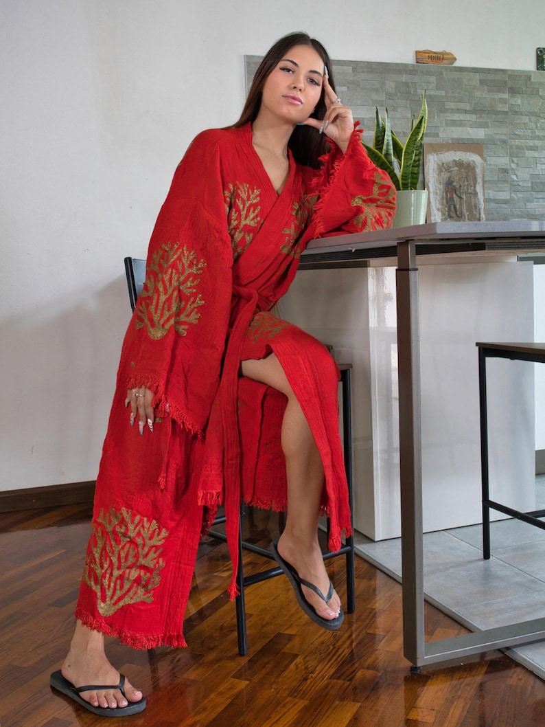 Op de afbeelding: Een rode kimono met gouden geborduurde koraalachtige ontwerpen. De kimono heeft een gefranjerde zoom en mouwen, en een bijpassende riem. De persoon draagt ​​zwarte slippers. De kimono is gemaakt van een lichte stof.