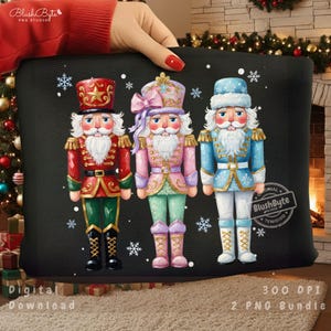 Może przedstawiać: Czarna poduszka z trzema kolorowymi postaciami dziadków do orzechów. Dziadki do orzechów mają czerwone, różowe i niebieskie mundury ze złotymi akcentami. Płatki śniegu są rozrzucone. Poduszka ma tekst "Digital Download" i "300 DPI 2 PNG Bundle".