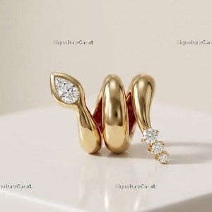 Könnte beinhalten: Ein goldener Ring mit einem glatten, geschwungenen Design, der an einem Ende mit einem birnenförmigen Diamanten und am anderen Ende mit einer vertikalen Reihe aus drei kleinen runden Diamanten besetzt ist. Der Text SignatureCarat ist sichtbar.