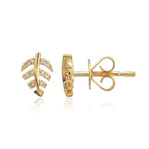 Peut inclure: Une paire de boucles d'oreilles à clous en forme de feuille dorée. Chaque boucle d'oreille présente un motif de feuille avec de petites pierres précieuses claires. Les boucles d'oreilles sont présentées sur fond blanc, mettant en valeur leurs détails et surfaces réfléchissantes.