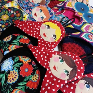 Può includere: Un set di presine in tessuto colorate con un tema di bambola russa annidata. Le presine sono realizzate in tessuto rosso, nero e bianco con pois e motivi floreali. Ogni presina ha un viso dipinto con un design rosso, bianco e nero.