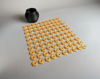 May include: A black, matte-finish ceramic vase sits next to a collection of small, gold-colored, hexagonal objects. Each object has a square center hole. The objects are arranged in a geometric pattern.