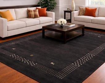 Puede incluir: Un salón con dos sofás blancos con cojines coloridos, una mesa de centro de madera oscura y una gran alfombra negra con un borde geométrico. La habitación tiene pisos de madera y una paleta de colores neutros.