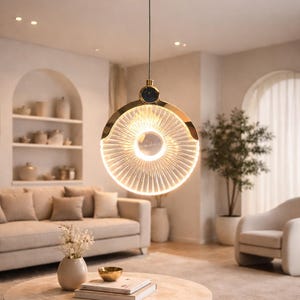 Könnte beinhalten: Eine moderne Pendelleuchte in Goldtönen mit einem kreisförmigen, gerippten Glasschirm. Die Leuchte hängt an einem dünnen Kabel und ist an einer goldenen Deckenhalterung befestigt. Das Innendesign weist neutrale Töne und eine minimalistische Ästhetik auf.
