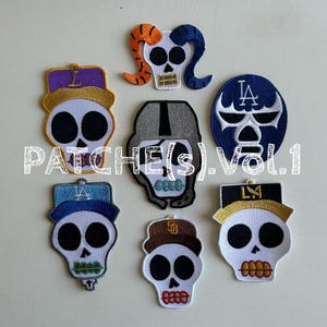 May include: A collection of seven skull patches with various designs. Each patch features a white skull with black eye sockets and a different hat or head covering. The patches include the text "PATCHES(S).VOL.1".