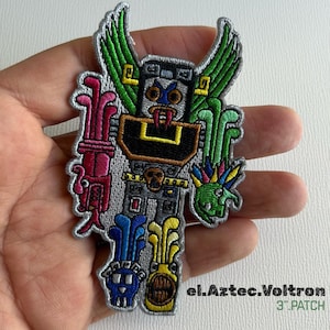 May include: Embroidered patch featuring a colorful Aztec-inspired robot design. The patch includes green, pink, blue, yellow, and gray elements with the text "el.Aztec.Voltron" and "3" PATCH". The patch measures approximately 3 inches.