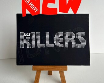 Peut inclure: Une impression rectangulaire noire sur un petit chevalet en bois. L'impression présente le texte LOS KILLERS en blanc, chaque lettre étant composée de petites icônes de crânes blancs. Au-dessus, le texte rouge NEW et 4X6.PRINT est affiché.