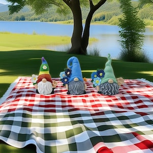May include: Three garden gnomes with colourful hats and beards sit on a red and white checked picnic blanket. One gnome has a rainbow hat, another a blue hat, and the third a green hat. Each gnome holds flowers.