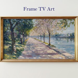 Op de afbeelding: Een ingelijst landschapsschilderij met een goudkleurige lijst. Het kunstwerk toont een pad met bomen langs een water. Het schilderij heeft de titel "Frame TV Art" in marineblauwe tekst.