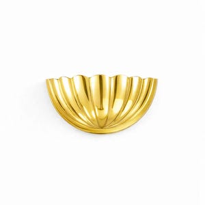 May include: A gold-colored, half-circle wall sconce with a scalloped edge. The sconce has vertical grooves and a reflective surface, mounted on a white wall. The design is reminiscent of a seashell.
