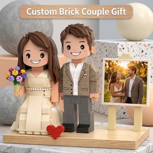 May include: A custom brick couple figurine set featuring a person in a cream-colored dress holding a colorful flower bouquet and a person in a brown blazer and gray trousers. A small red heart and a framed photograph of a couple are included.