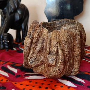 Può includere: Un piccolo vaso rotondo e testurizzato con una finitura in bronzo metallizzato che imita l'aspetto della corteccia d'albero ruvida. Il contenitore presenta un centro profondo e aperto e una superficie esterna irregolare con creste verticali.
