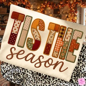 May include: A cream-colored sweatshirt featuring the embroidered text 'TIS THE' in large, block-style letters filled with various autumn-themed fabric patterns, and the word 'season' in brown cursive script underneath the block letters.