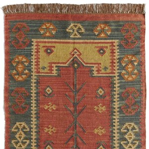 May include: A rectangular rug with a red central field featuring a tree-like design. The rug has a blue border with repeating geometric patterns in orange and yellow. The top edge has a brown fringe.