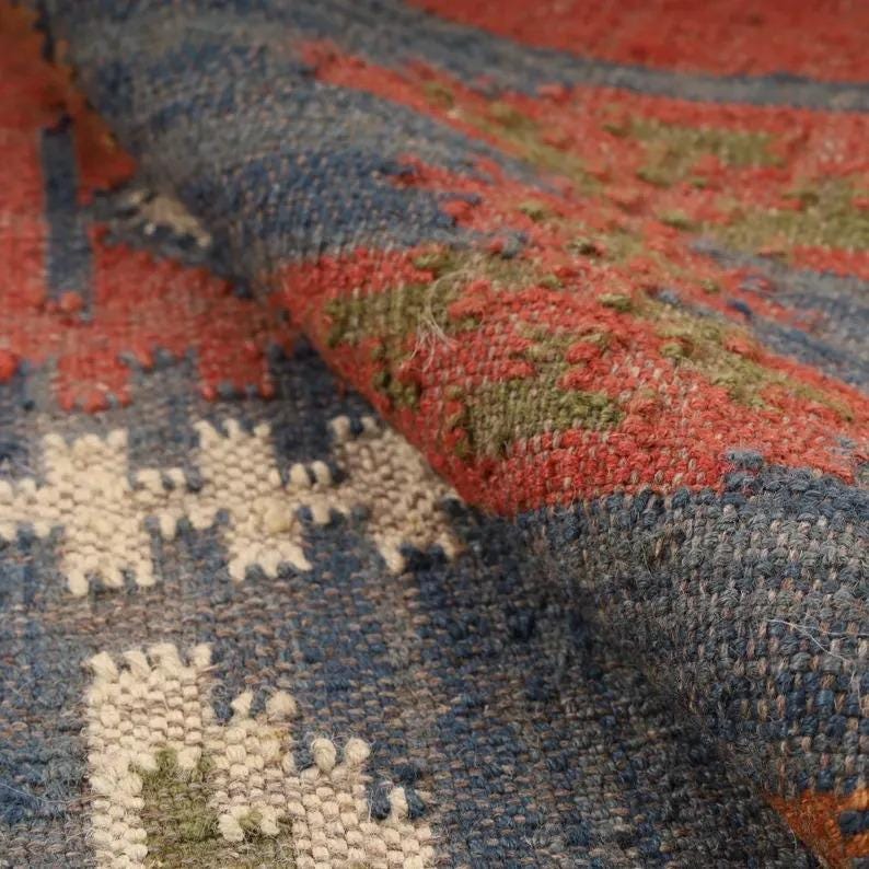 May include: Close-up of a woven rug with a geometric pattern. The rug features a combination of red, blue, white, and green hues. The texture of the rug is visible, showcasing the woven fibers and the intricate design.