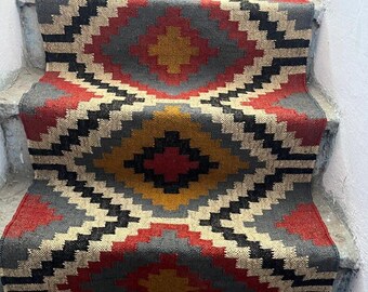 May include: A stair runner with a geometric pattern in red, gray, black, and yellow. The rug is installed on concrete steps. The design features diamond shapes and zig-zag lines, creating a bold, eye-catching look for home decor.