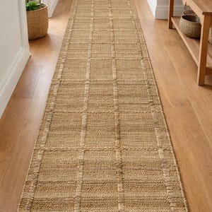 May include: A long, rectangular jute runner rug with a grid design, laid on a wooden floor. The rug is approximately 90 cm wide and 240 cm long. The natural tones of the rug complement the wooden flooring, creating a warm, inviting hallway.
