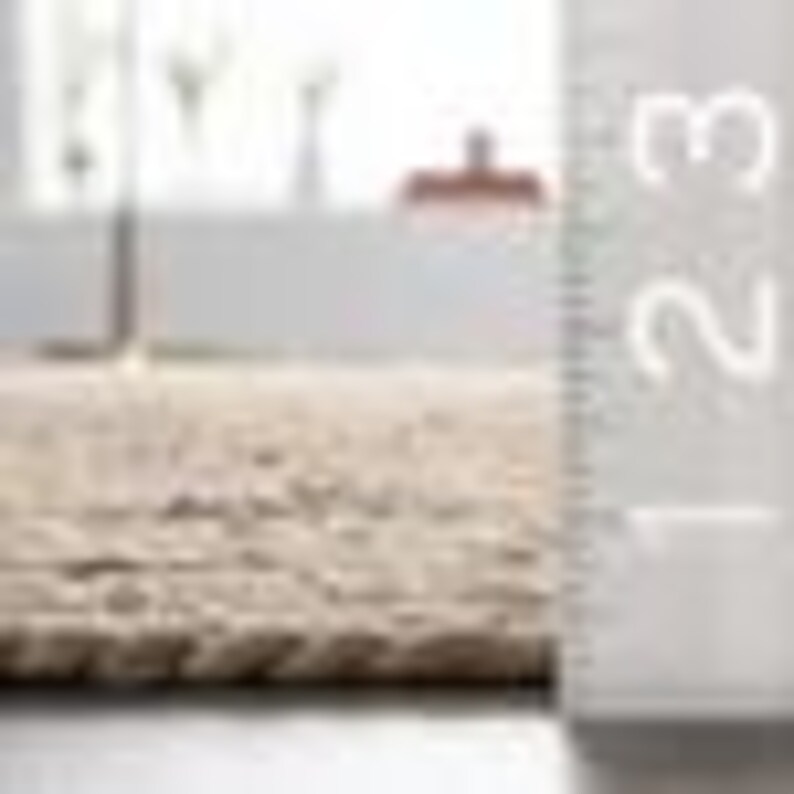 May include: Close-up of a beige woven rug with a textured surface. The rug appears to be made of natural fibers. A ruler is positioned vertically along the edge, indicating a thickness of approximately 1 inch.